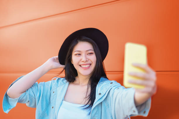 Happy Asian girl taking selfie with mobile smart phone outdoor - Trendy influencer having fun with new trends social networks apps - Millennial generation lifestyle people addicted technology Happy Asian girl taking selfie with mobile smart phone outdoor - Trendy influencer having fun with new trends social networks apps - Millennial generation lifestyle people addicted technology auto post production filter stock pictures, royalty-free photos & images