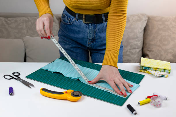 istock woman in a yellow measures fabric tissue. there are quilting tools on the table. patchwork knife, scissors, lined cutting mat, self-locking, thread, centimeter tape. sewing supplies 1219786265