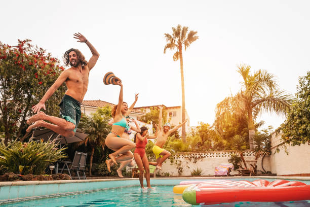 istock Group happy friends jumping in pool at sunset time 1219786311
