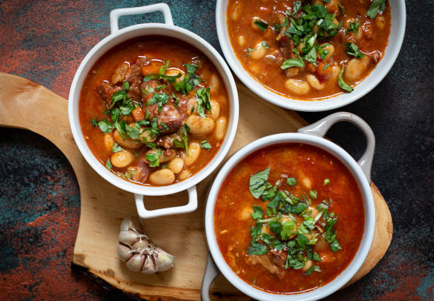Bean soup with meat and vegetables served on a rustic board with garlic. Traditional Balkan soup or stew Corbast Pasulj (Grah). Top view, copy space