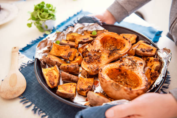 istock Male hands putting baking sheet with roasted grilled orange pumpkin butternut squash halfs and sweet potato slides with herbs on blue napkin. Vegetarian and vegan food diet. Healthy eating concept. 1219788234