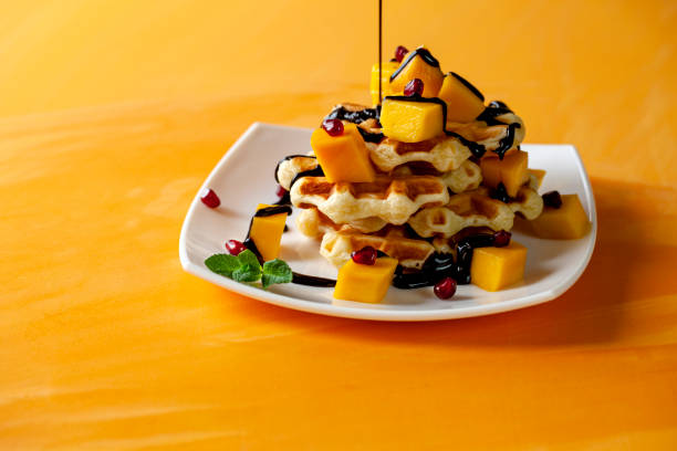 венские с мороженым и ломтиками манго, облизанные шоколадом, на оранжевом фоне - autumn banana breakfast close up стоковые фото и изображения
