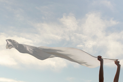 woman holds a white scarf that flies in the sky; freedom concept