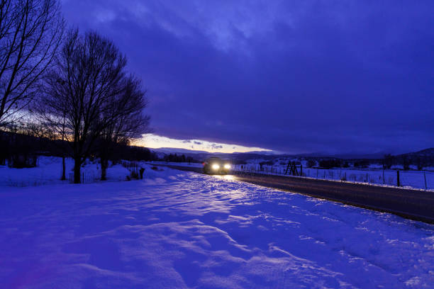 Car Driving Down Road at Night During Snow Storm - Car blur with lights going by on wet road with fresh snow coming down. Night driving at dusk during blue hour.
