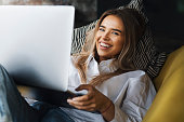 Cheerful young lady holding laptop while laying on couch. Girl relaxing after work, using internet connection