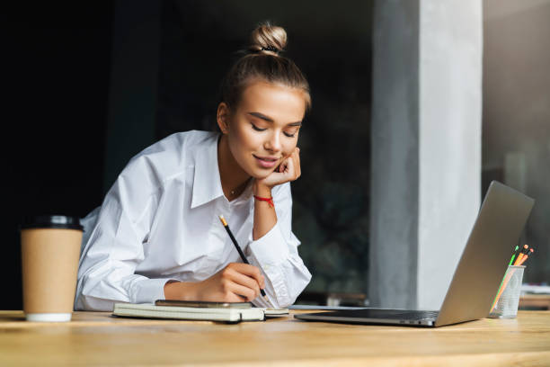 istock Student preparing for seminar, writing notes in copybook, searching for information online. Female working 1219797345