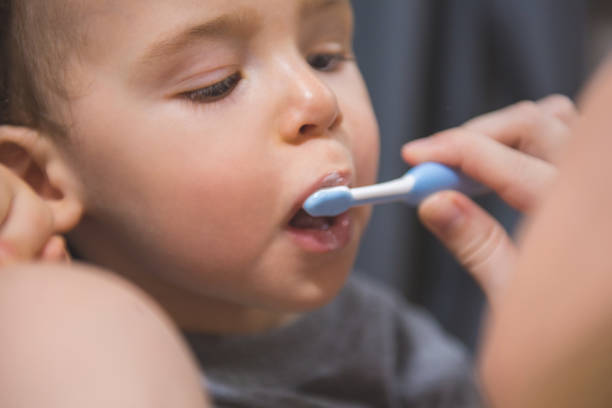 Child first time brushing his teeth with a help from his mother