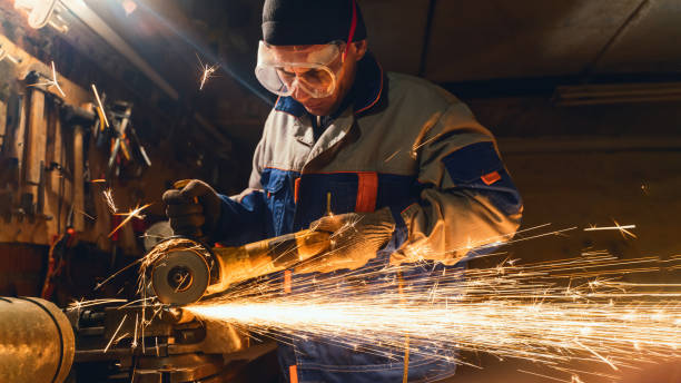 istock Locksmith in special clothes and goggles works in production. Metal processing with angle grinder. Sparks in metalworking 1219808305