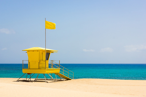Nobody on turquoise sea with yellow flag on top of baywatch station on sunny day. Summer vacation concept