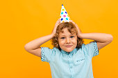 Little boy with curly hair in blue shirt and shorts is happy because have b-day isolated on yellow background