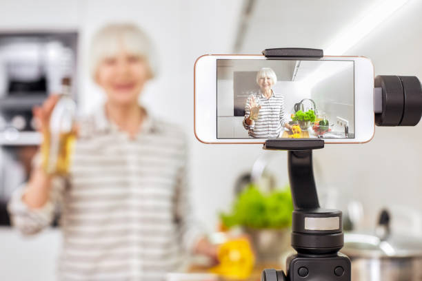 pensionista usando smartphone moderno, gravando vídeo online - women home video camera camera vitality - fotografias e filmes do acervo