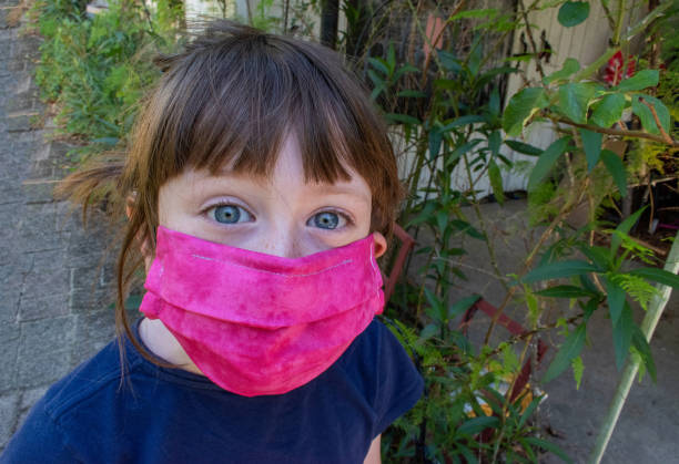 young girl in bright pink protective face mask outside near plants