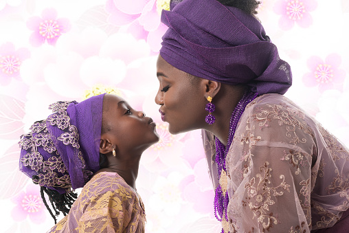 Portrait in profile of a mother and child girl kissing. African traditional purple clothing on flowered background