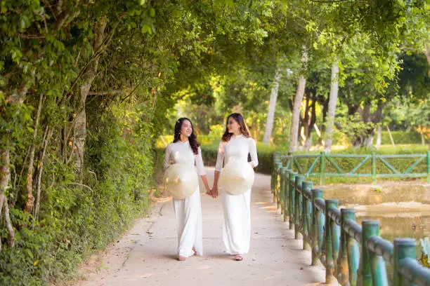 Two Vietnamese girls wearing a white Ao Dai and holding a conical hat at Hoang Tru, Kim Lien, Nam Dan. The Ao dai ( long-dress Vietnamese) is traditional costume of Vietnamese woman
