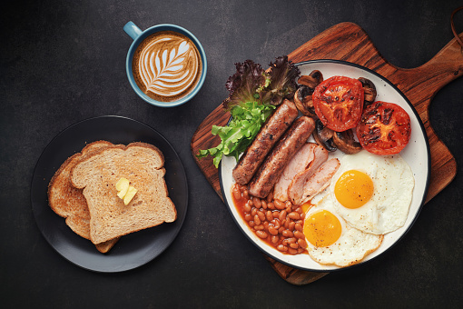 Full English Breakfast with Latte Art on dark table sausage eggs bean bacon tomato mushroom