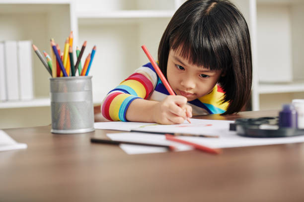 Drawing little girl Adorable talented Asian girl sitting at desk at home and drawing with red pencil Coloring stock pictures, royalty-free photos & images