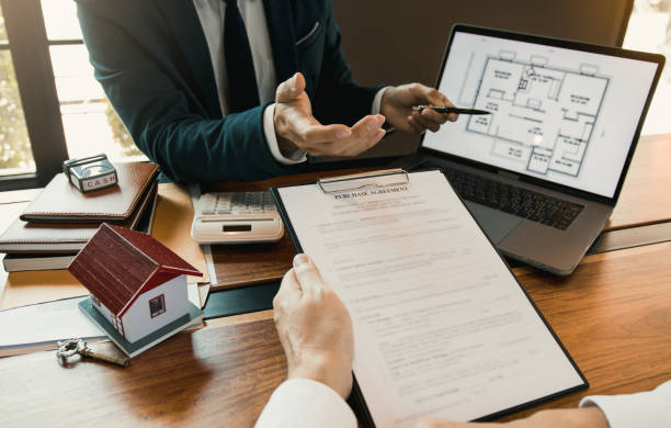istock Agents are using pens pointing to blueprint home design on laptop screen and being explained to customers at the office. 1219838683
