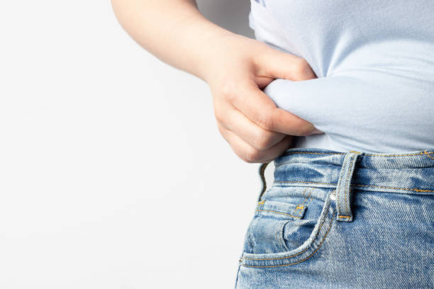 Girl holds belly fold on a white background, concept of excess weight Girl holds belly fold on white background, concept of excess weight pot belly stock pictures, royalty-free photos & images