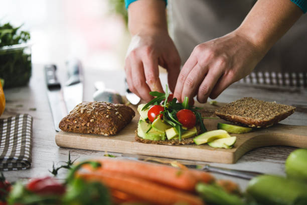 Adding fresh cherry tomatoes to healthy vegan sandwich Close up of female hands adding cherry tomatoes to a vegan sandwich made with arugula, avocado and brown bread. making a sandwich stock pictures, royalty-free photos & images