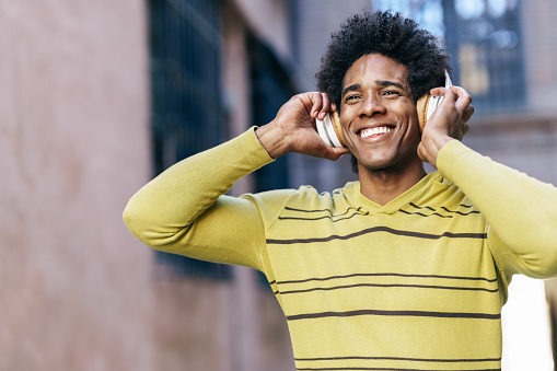 Black man with afro hair listening to music with wireless headphones sightseeing in Granada, Andalusia, Spain.