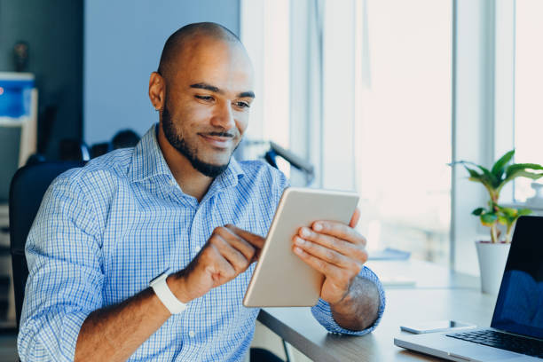 istock Handsome cheerful african american man in creative atmosphere using laptop sitting on a wooden table. 1219847956