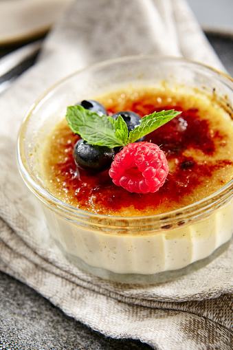 Classic creme brulee in glass bowl. Appetizing ice cream close up. Delicious dessert with blueberry and raspberry, Sugary meal with caramel, mint and berries decoration. Restaurant sweet food