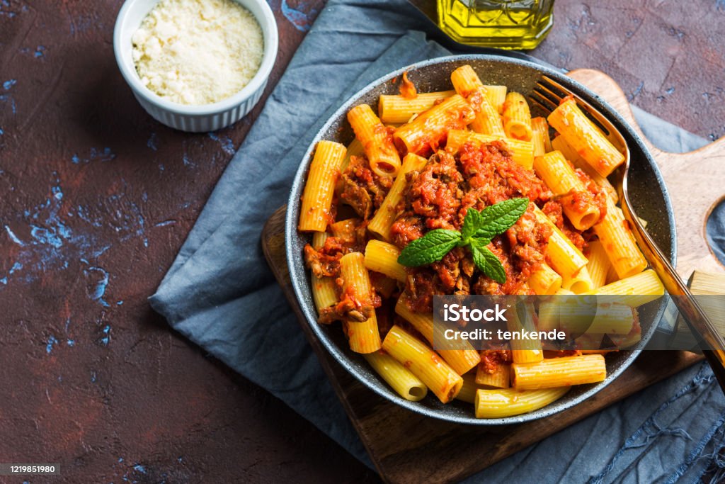 Delicious pasta with italian tomato meat sauce Delicious rigatoni pasta with italian tomato meat ragu sauce served in a pan on dark brown background. Traditional pasta dish concept. Home made lunch Rigatoni Stock Photo