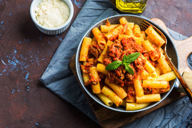 Delicious pasta with italian tomato meat sauce Delicious rigatoni pasta with italian tomato meat ragu sauce served in a pan on dark brown background. Traditional pasta dish concept. Home made lunch rigatoni stock pictures, royalty-free photos & images