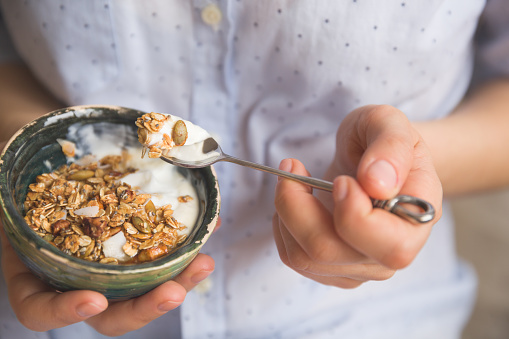 Young woman with muesli bowl. Girl eating breakfast cereals with nuts, pumpkin seeds, oats and yogurt in bowl. Girl holding homemade granola. Healthy snack or breakfast in the morning.