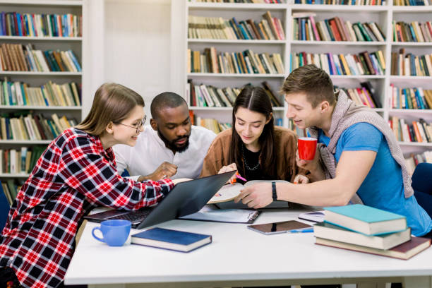 istock Young multiethnical college students at the library studying together, they are smiling, looking at book while finding new useful information for their exam or home task 1219859889