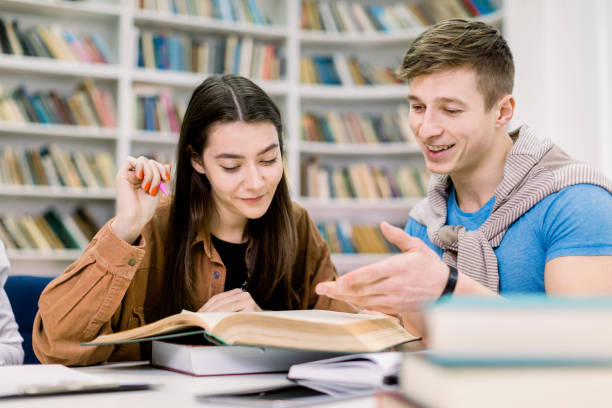 istock Students, Caucasian handsome boy and pretty girl, sitting at a table in a library while reading books and learning together, discussing their home work or exam preparation. Education, friendship 1219859913