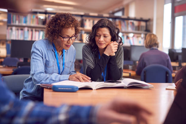 lehrer mit reifen weiblichen erwachsenen student sitzen am tisch arbeiten in college-bibliothek - adult student women mature adult library stock-fotos und bilder