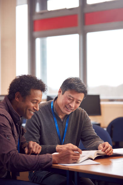 insegnante con studente adulto maschio maturo seduto a tavola a lavorare nella biblioteca del college - mature adult men male african descent foto e immagini stock