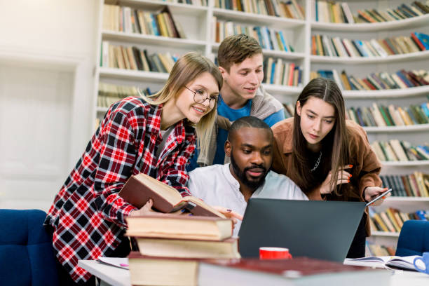 istock Four joyful multiracial students in library which are studying together and preparing for exams, using laptop for internet searching of information. Education, learning, library concept 1219861081