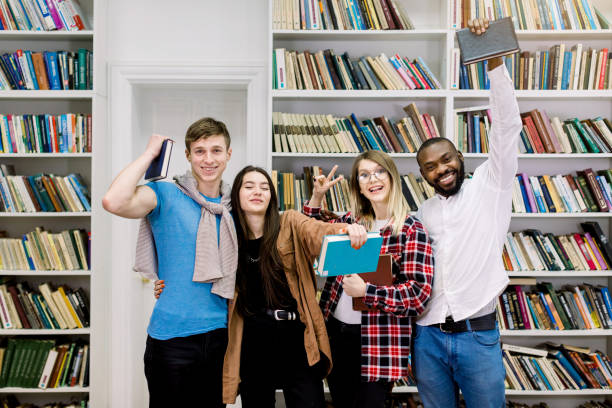 istock Students in library, happy learning and education. Young people with books in library are studying and having fun together, posing on camera, smiling and gesturing 1219861214