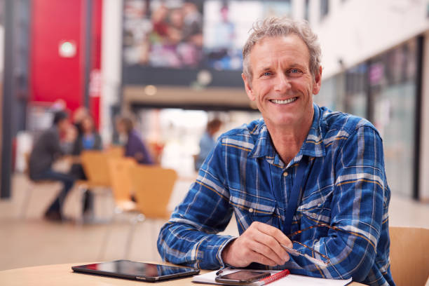 portrait of mature male teacher or student with digital tablet working at table in college hall - night school imagens e fotografias de stock