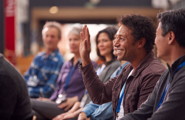 istock Businessman In Presentation At Conference Raising Hand To Ask Question 1219862961