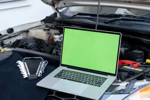 Photo of Laptop computer on car hood for engine diagnostic. Car garage repair service concept.