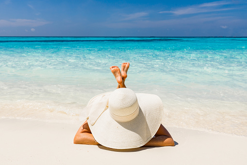 Woman with sun hat sunbathing during summer day on the beach. Copy space.