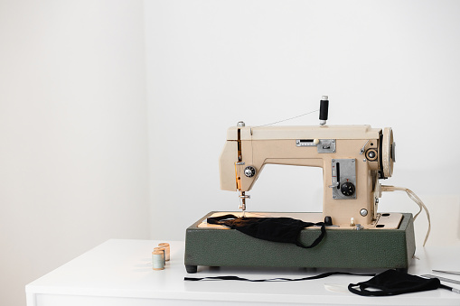 Beige vintage sewing machine the process of sewing a protective medical mask at home workplace on white isolated background