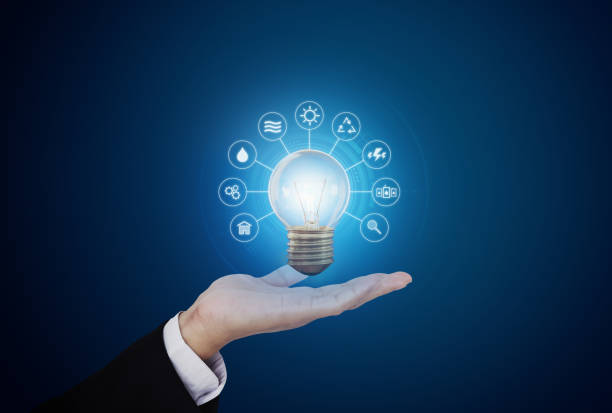 istock Hand holding bright light bulb with energy resources icon, on blue background. Energy concept 1219876597
