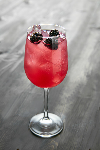 A glass of Sangria blueberry cocktail with ice on a wooden table side view, isolated