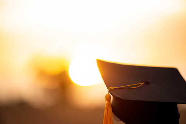 Close up Black Graduation Cap and Golden Yellow Tassel on Sunset Background And has a golden beam. Close up Black Graduation Cap and Golden Yellow Tassel on Sunset Background And has a golden beam. masters degree photos stock pictures, royalty-free photos & images