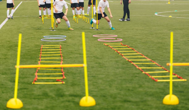 Soccer field with training equipment and players with coach in background. Junior football team training and coach. Sport team on training. Football training equipment: ladder, hula hoop, hurdle, cone Soccer field with training equipment and players with coach in background. Junior football team training and coach. Sport team on training. Football training equipment: ladder, hula hoop, hurdle, cone sports training drill stock pictures, royalty-free photos & images