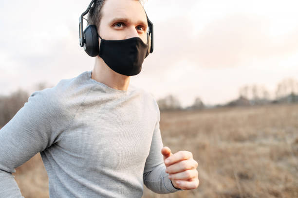 Guy in a medical mask is jogging Sport during quarantine, self-isolation in the countryside. A young athletic guy is jogging on a dirt road in the meadow. He is wearing a black medical mask and headphones human cardiopulmonary system audio stock pictures, royalty-free photos & images