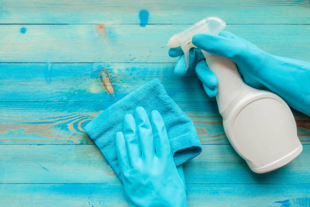 Hands in rubber gloves holding blue microfiber cleaning cloth and cleaning bottle with spraying liquid stock photo