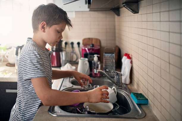istock Little boy washing dishes at home 1219893279