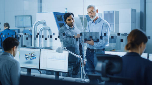 istock Automotive Design Factory: Project Manager, Chief Mechanical Engineer Talk, Use Laptop, Discuss Project Details. High-Tech Industrial Facility Construction of Engines using CNC Machinery. 1219894330