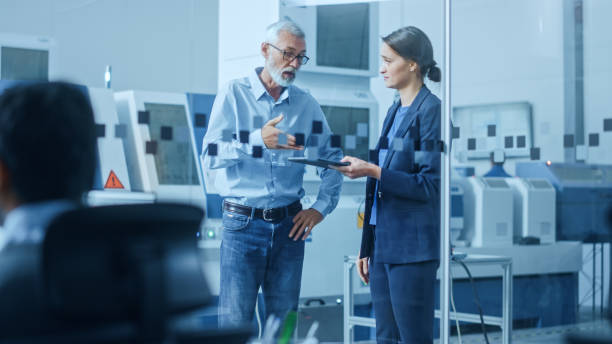 istock Modern Factory: Female Engineer, Male Project Manager Standing in High Tech Development Facility, Talking and Using Tablet Computer. Contemporary Facility with CNC Machinery, Robot Arm Production Line 1219894344