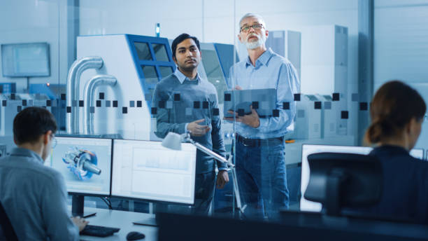istock Automotive Design Factory: Project Manager, Chief Mechanical Engineer Talk, Use Laptop, Discuss Project Details. High-Tech Industrial Facility Construction of Engines using CNC Machinery. 1219894404
